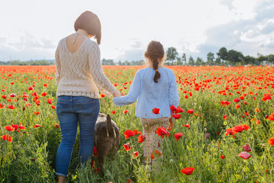 Rear view of mother and daughter walking away in the poppy field with their dog following them