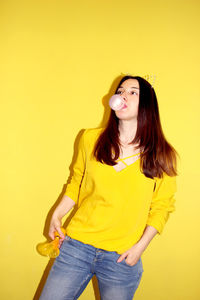 Beautiful young woman standing against yellow wall