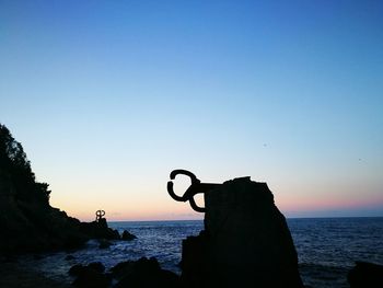 Silhouette people on cliff in front of sea against clear sky