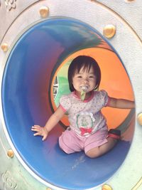 Portrait of happy boy sitting on slide at playground