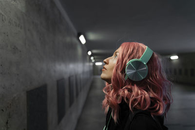 Woman with pink dyed hair listening music through headphones