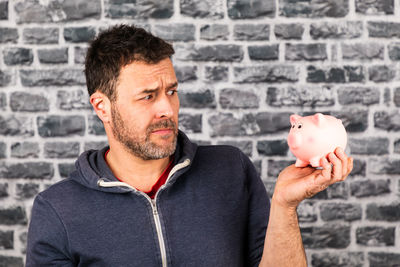 Man holds a piggy bank in his hand against a stone wall