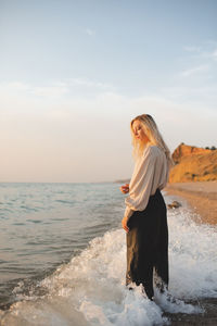 Elegant young woman wear stylish black pants and shirt standing in sea water over coast line outdoor