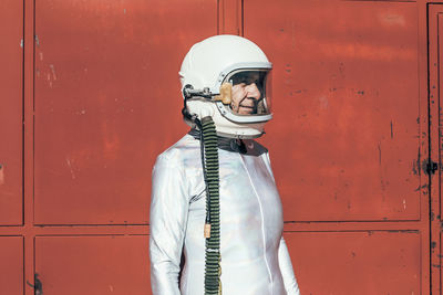 Man in spacesuit standing near red wall of industrial facility on sunny day