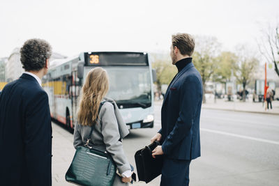 Female entrepreneurs with male coworkers looking at bus while standing in city