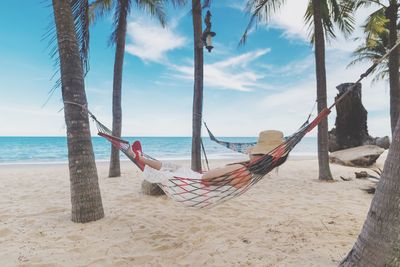 Full length of woman resting in hammock at beach against sky