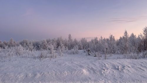 Snow covered land against sky during sunset