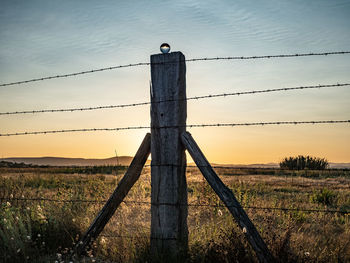 Fence on field against sky during sunset