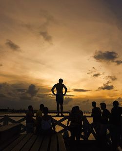 Silhouette people standing by sea against sky during sunset