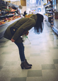 Side view of woman bending over floor at supermarket