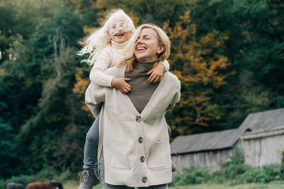 A little laughing girl is having fun with her mother sitting on her back.