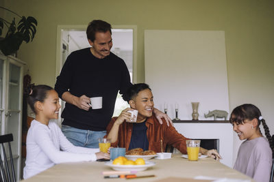 Happy gay parents enjoying breakfast with daughters while sitting at dining table in home