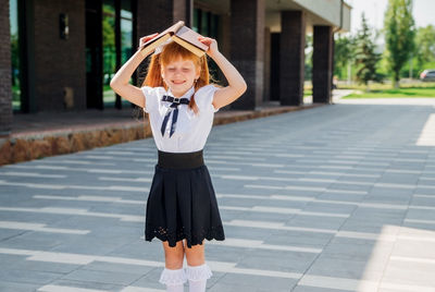 Funny charming little girl with a book on her head, on the first day of school or kindergarten.