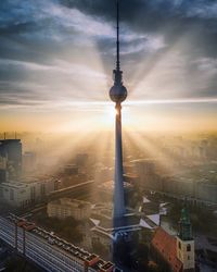 Communications tower in city against sky during sunset