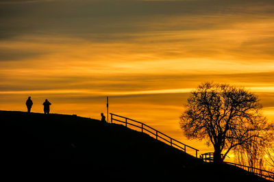 Silhouette person standing by tree against orange sky