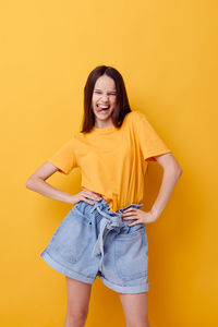 Portrait of young woman standing against yellow background