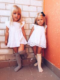 Thoughtful sisters wearing white dresses while standing against wall