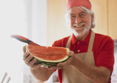 Portrait of senior man holding watermelon at home