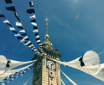 Low angle view of bird flying by clock tower with buntings against sky