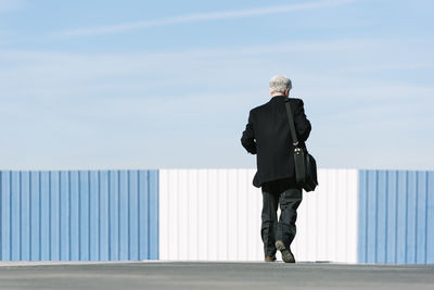 Rear view of businessman walking on road against sky