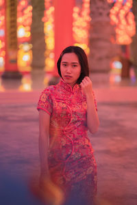 Portrait of beautiful young woman standing against illuminated blurred background