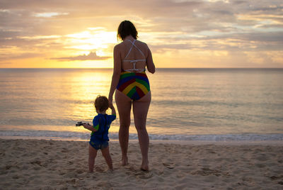 Rear view of mother and daughter on beach during sunset