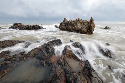 Long exposure image of waves crashing at beach against storm clouds