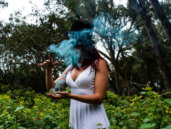 Woman stirring up blue smoke in garden 