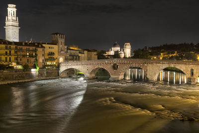 Arch bridge over river against buildings in city at night