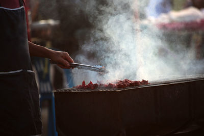 Man with serving tong preparing food on barbecue grill