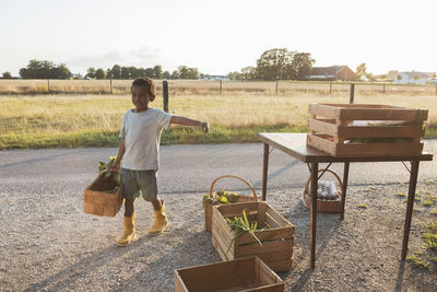 Boy carrying vegetable basket while walking at roadside