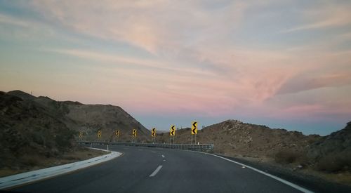 Road by mountains against sky during sunset
