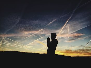 Silhouette man igniting cigarette standing on field against sky during sunset