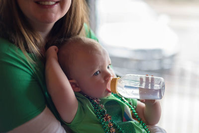 Midsection of woman carrying daughter drinking water from baby bottle