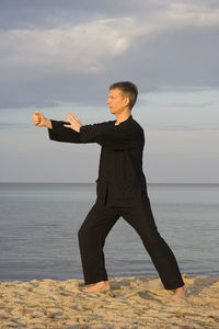 Man practicing martial arts at sandy beach against sky