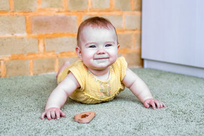 Portrait of smiling little caucasian baby girl in yellow dress with wooden teething toy.