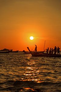 Silhouette people on sea against orange sky during sunset