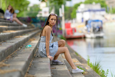 A portrait of a pretty young woman taken in the summertime in a city sitting on a staircase.