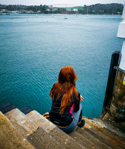 Rear view of woman looking at sea while sitting on staircase