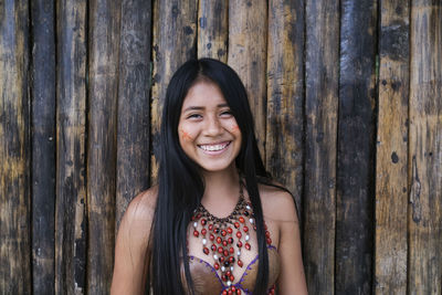 Portrait of smiling woman standing against wooden wall