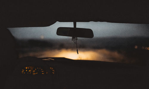 Silhouette rear-view mirror against windshield in car during sunset