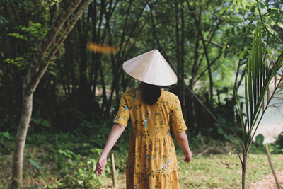 Rear view of woman wearing asian style conical hat walking in forest