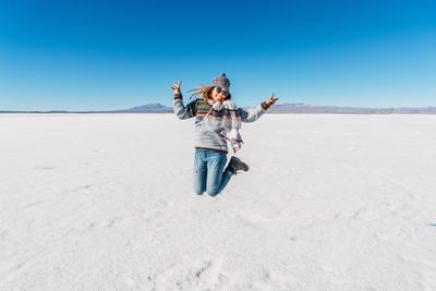 Young woman standing on desert against clear blue sky