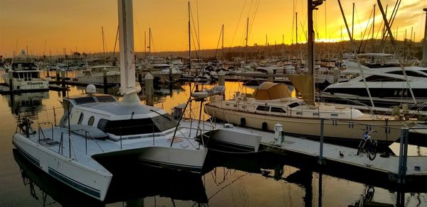 Sailboats moored in harbor at sunset