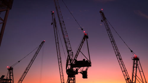 Low angle view of cranes against sky at sunset