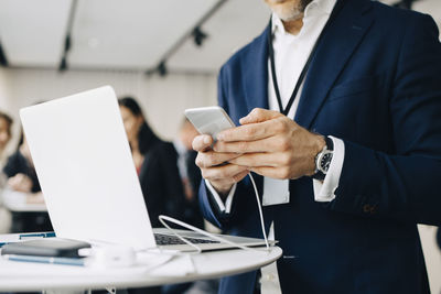 Midsection of male entrepreneur using phone while standing in office seminar