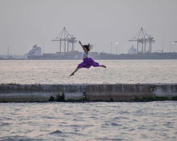 Woman jumping in sea against clear sky