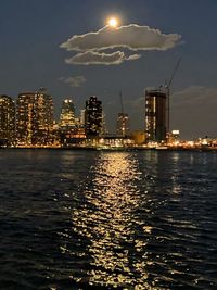 Illuminated buildings by sea against sky at night