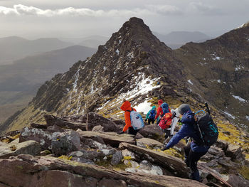 People on rocks by mountains against sky