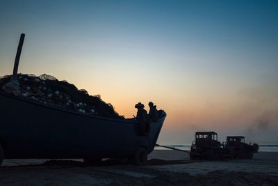 Silhouette man standing on boat at beach against clear sky during sunset